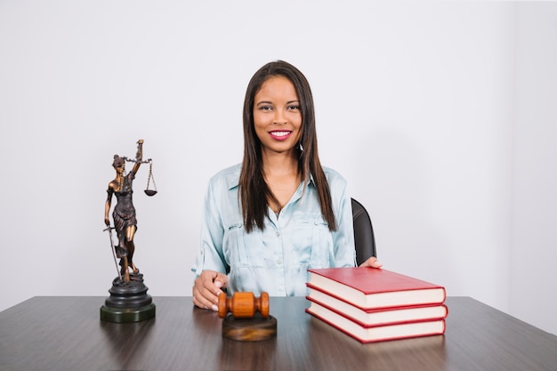 Free photo cheerful african american woman at table with gavel, books and statue